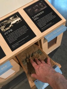 The museum display has a piece of jute fabric and a descriptive placard.